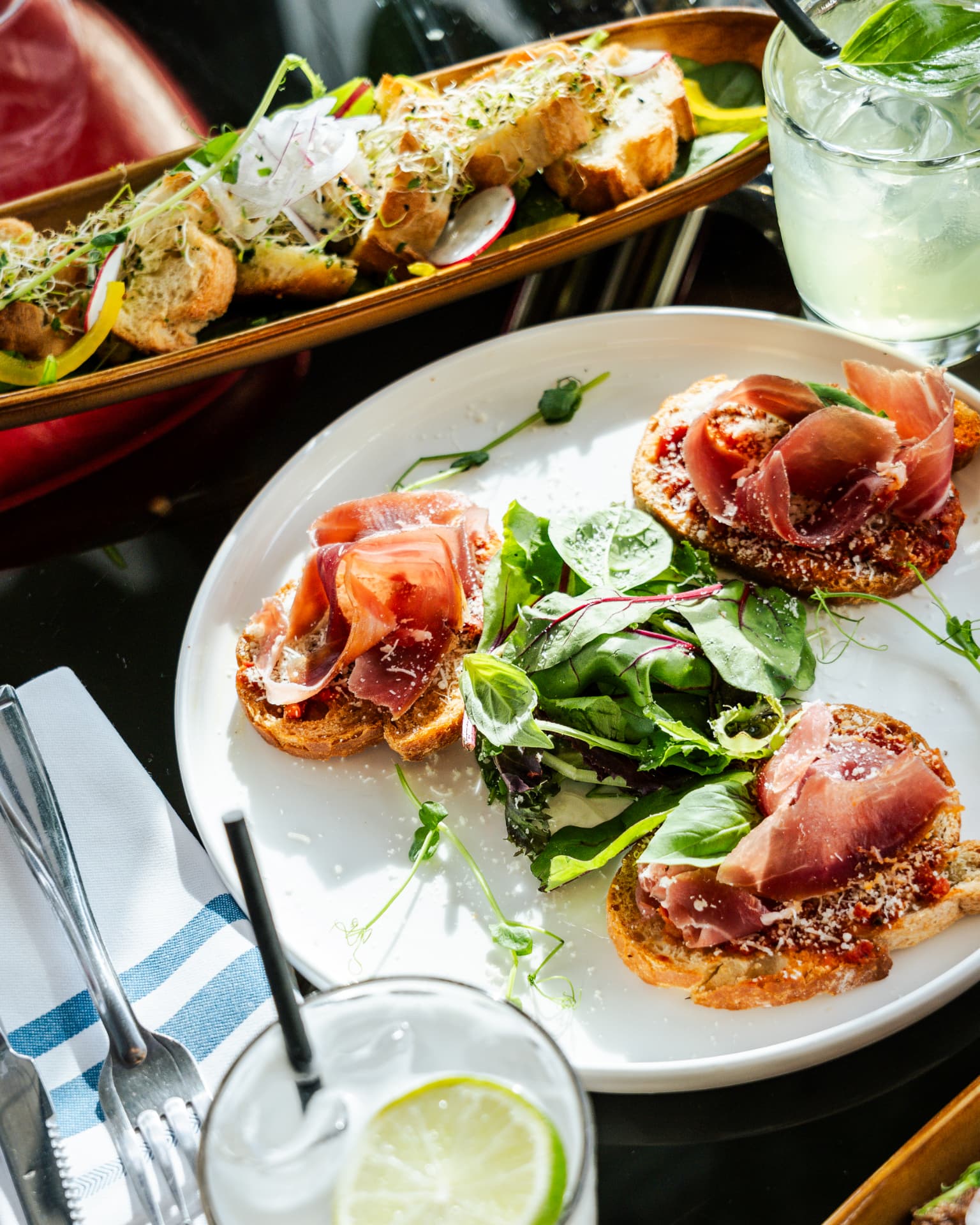 Tartines de jambon cru et jeunes pousses servies en terrasse avec un cocktail